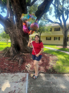 Sadith Mendoza standing on a sidewalk in front of Poinciana Condominiums holding balloons